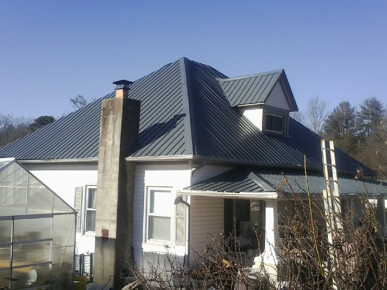 Dark blue standing seam metal roof on a white farmhouse with dormer — Slate & Tile Roof Repair by Roofing Brothers in Ecorse