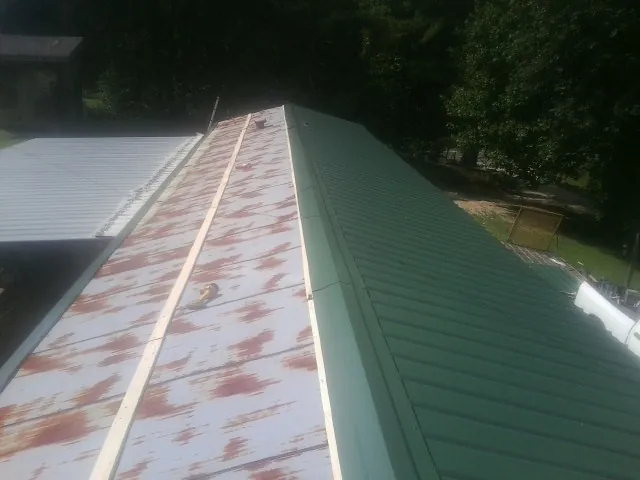 Old rusted panels beside newly installed green metal roofing — Wind Damage Roof Repair by Roofing Brothers in Ecorse