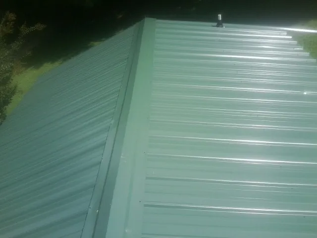 New green metal panels meeting at the ridge of a roof — Flat Roof Repair work by our crew in Ecorse