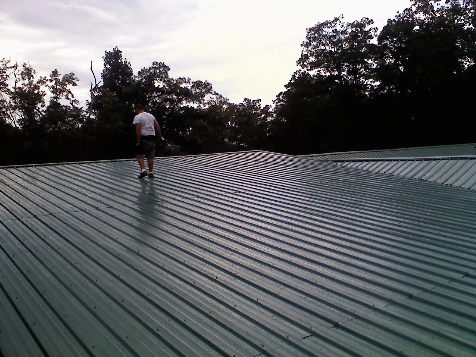 Roofer walking a wide expanse of new green metal roofing in Ecorse