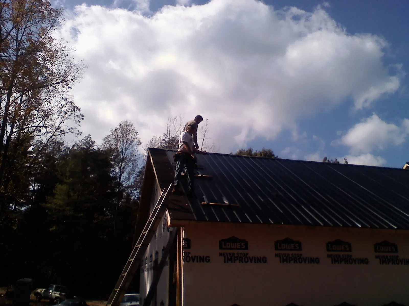 Roofer fastening dark metal panels high against a cloudy sky, from a Roof Inspection job in Ecorse